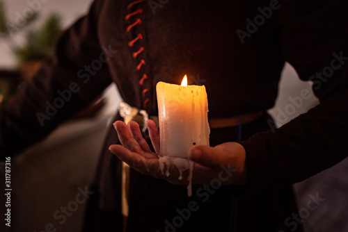 A woman dressed in a medieval dress holds a burning white candle in her hand. Mystery witch