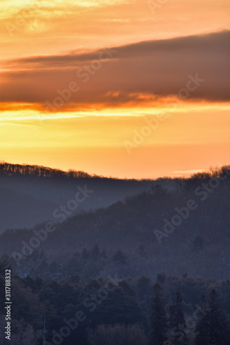 Cold Sunrise Over Tree Covered Hills And Frozen Water With Snow At Red House Lake, Allegany State Park, New York