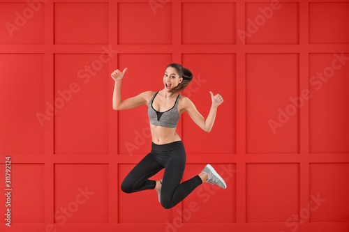Sporty jumping young woman showing thumb-up gesture against color background