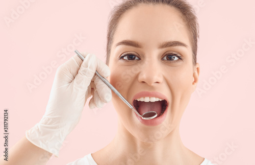 Dentist examining teeth of beautiful young woman against color background