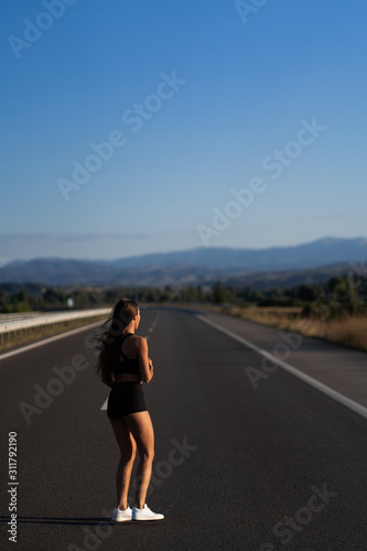 Young girl running along the road. Athletic happy woman jogging in trendy black sexy top and shorts enjoying the sun exercising. Healthy lifestyle. Perfect fitness body shapes and tan skin © MONIUK ANDRII