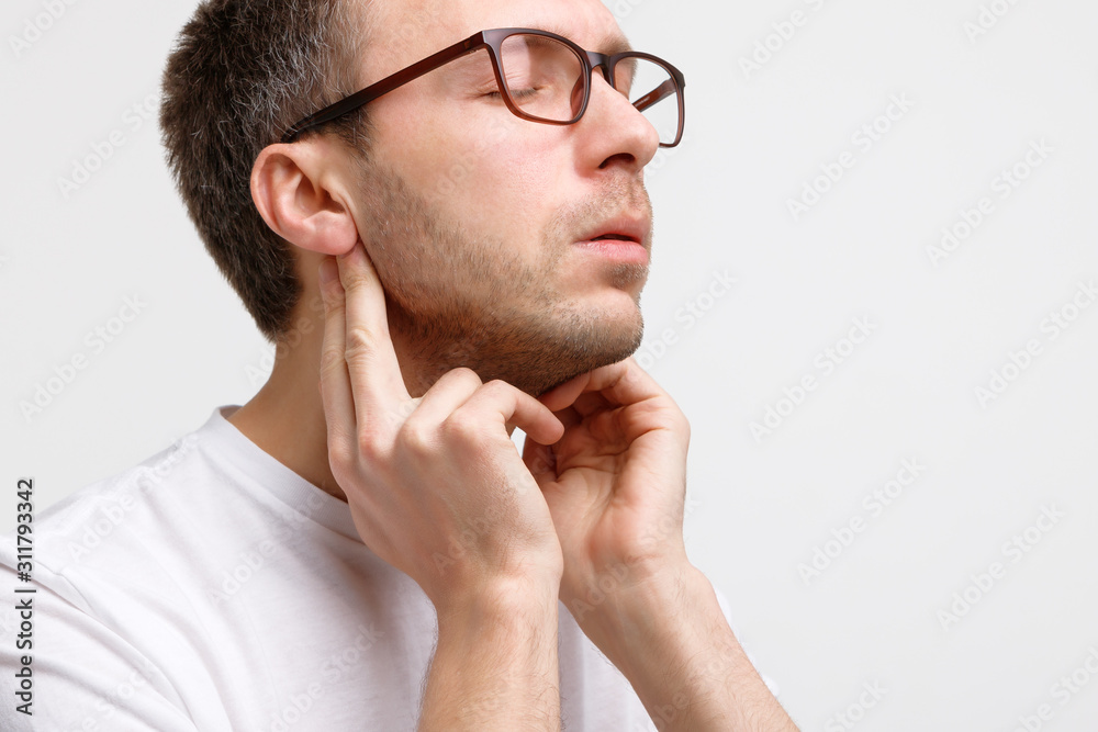 Close up portrait of sick man touches the lymph glands with his fingers near the ear, suffering from pain, closed eyes, isolated. Lymphadenitis, immunity weakened after illness, otitis. Close up portrait of sick man touches the lymph glands with his fingers near the ear, suffering from pain, closed eyes, isolated. Lymphadenitis, immunity weakened after illness, otitis.