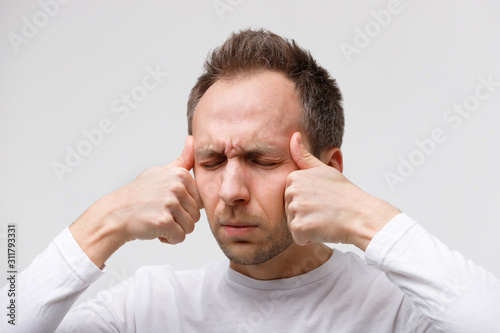 Body vertigo, nervous tension, temporal and throbbing pain concept. Close up portrait of man massaging his temples, closed eye, isolated on gray background. Strong migraine. 