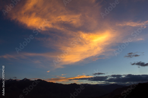 bright clouds in the dark sky over the silhouettes of mountains with snowy peaks