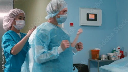 Nurse and assistant dressing surgeon gown in surgery room