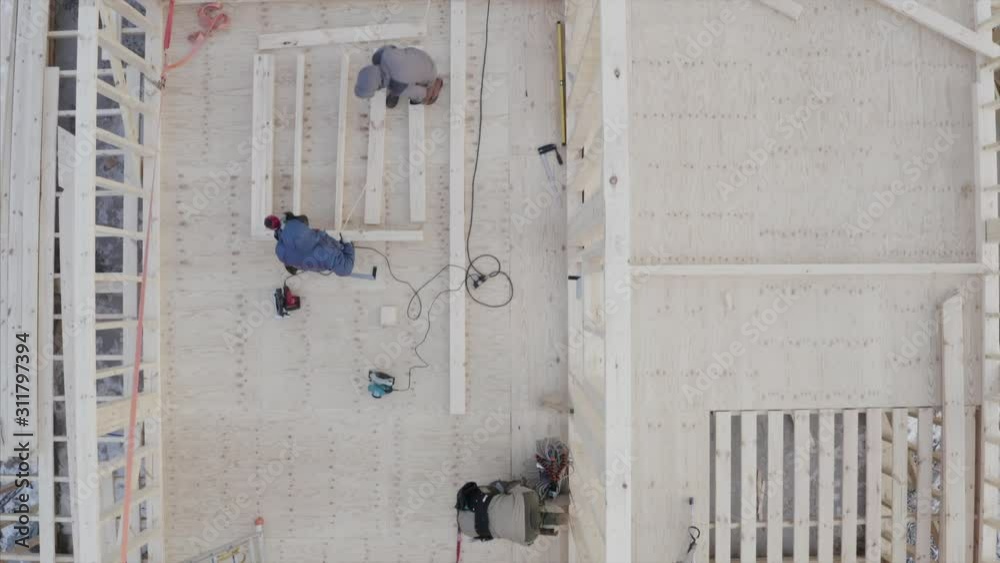 Flying above unfinished wooden frame house, top aerial view of builders working on the second floor Flying above unfinished wooden frame house, top aerial view of builders working on the second floor