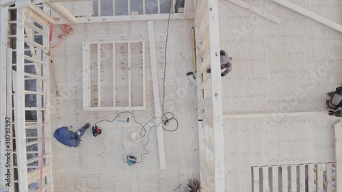 Top ascending aerial view of incompleted residential frame house and team builders working on the second floor photo