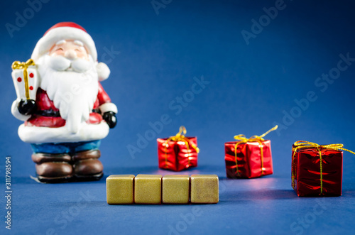 Four blank gold cubes in front of Santa Clause figure and gifts in a conceptual image. Over blue background.
