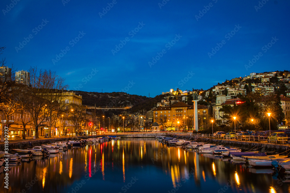 Rijeka, Croatia / December 10th 2018: Boats in river Rjecina and Delta in sunset and blue hour