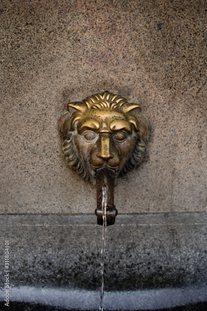 Old venetian fountain with lion heads springs pure drinking water in SOFIA BULGARIA August 12, 2019. Close up stone fountain bowl and mouth of a golden lion fountain. selective focus