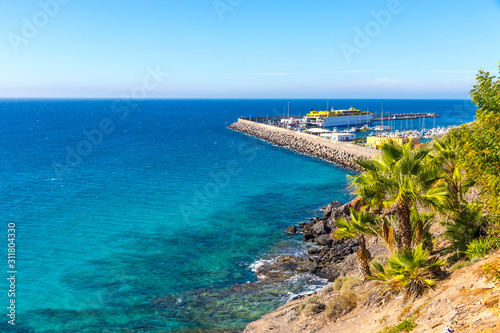 Azure water of Atlantic ocean on Morro Jable beach, Fuerteventura island, Canary Islands, Spain. Port of Morro Jable  in a distance © katatonia