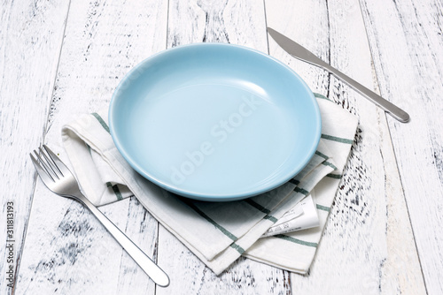 Blue Plate with utensils and dish towel on white wooden background side view