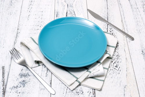 Blue Plate with utensils and dish towel on white wooden background side view