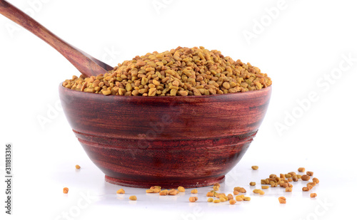 Fenugreek seeds in wooden bowl with spoon isolated on white background photo