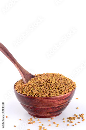 Fenugreek seeds in wooden bowl with spoon isolated on white background photo