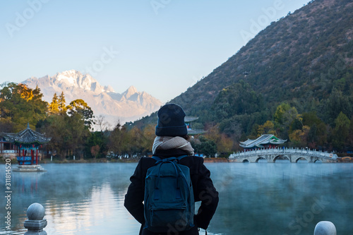 Young woman traveler traveling at Black Dragon Pool with Jade Dragon Snow Mountain background, landmark and popular spot for tourists attractions near Lijiang Old Town. Lijiang, Yunnan, China