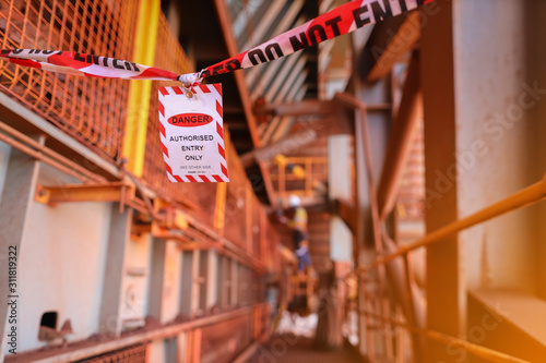 Red and white danger tag exclusion zone tape with sign barricade working area off as dropped object zone high risk work with defocused worker background construction site, Perth city Australia 