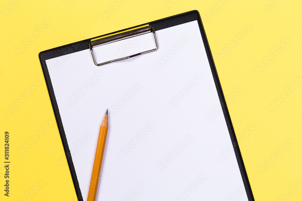 Clipboard with white sheet and pen on a yellow background. View from above. space for text Clipboard with white sheet and pen on a yellow background. View from above. space for text