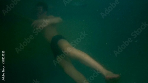 Muddy water. The masked teenager dives and swims underwater in the pool. Air bubbles around the body. The guy in swimming trunks.