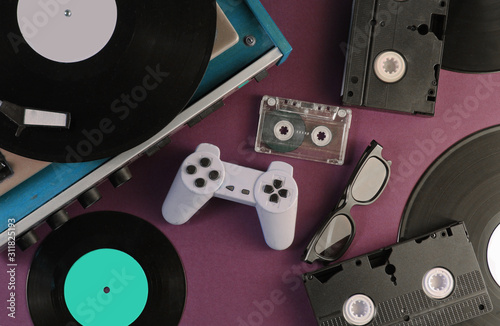 Retro media and entertainment items 80s. Vinyl player, Video, audio cassettes, 3D glasses, gamepad on red background. Top view