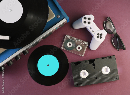Retro media and entertainment items 80s. Vinyl player, Video, audio cassettes, 3D glasses, gamepad on red background. Top view