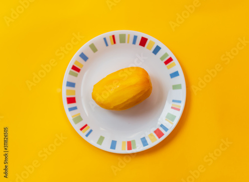 One peeled mango fruit on a white plate kept on a yellow background. Single fresh mango without skin isolated icon with solid color backdrop. Skinless uncut whole fruit flat lay layout template. photo