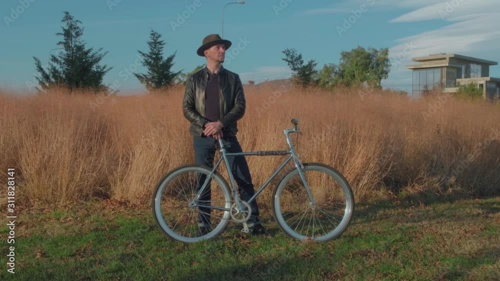 Portrait of a stylish man in a hat with a retro bike standing in the Park and looking at the camera. The camera zooms in. Portrait of a stylish man in a hat with a retro bike standing in the Park and looking at the camera. The camera zooms in.