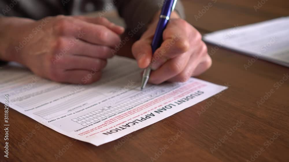 The man signs students loan application paper form document. Student finance. Paying for post-secondary education and the associated fees, such as tuition, books and supplies, and living expenses