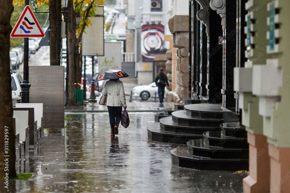 Fototapeta premium Rainy weather in the city. People walk under umbrellas during light rain on the wet streets of the city.