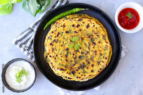 A Food called Methi paratha or Methi thepla is a Indian breakfast dish served with curd and ketchup. with copy space.