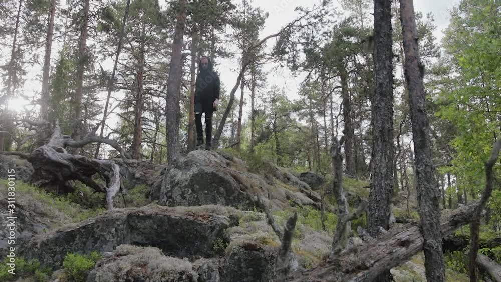 Stylish European man in a black cardigan and sunglasses descends a rocky cliff in the woods and jumps down. Travel concept Stylish European man in a black cardigan and sunglasses descends a rocky cliff in the woods and jumps down. Travel concept