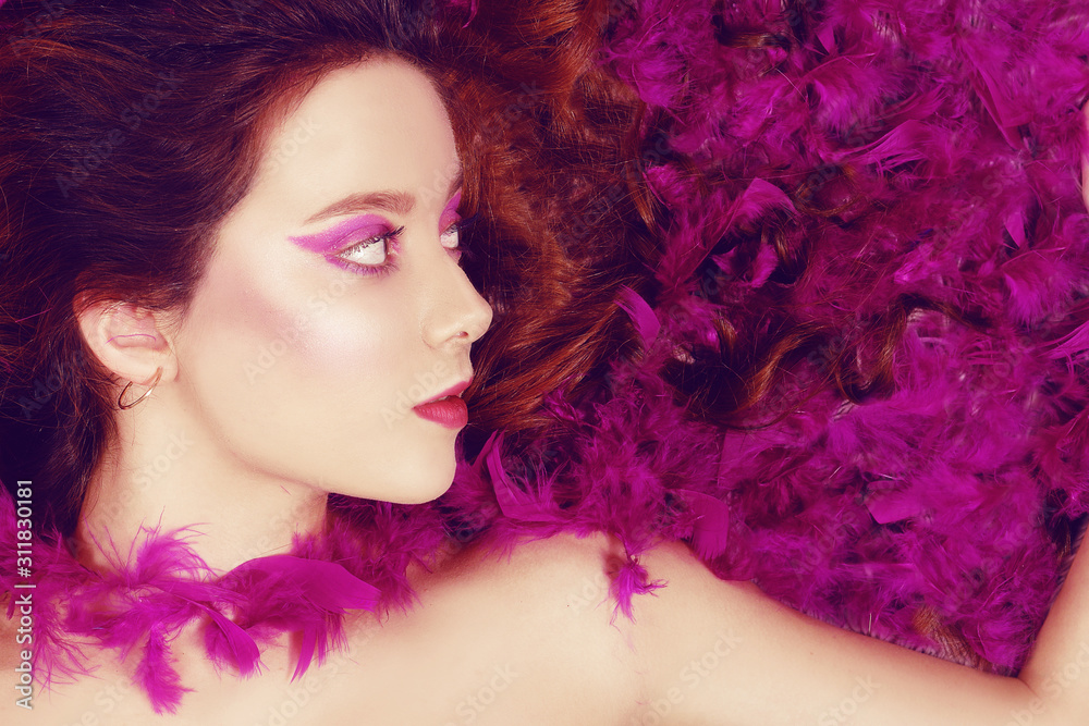 Beautiful young brunette lies with closed eyes in pink feathers. Girl with pink / purple make-up. Beauty. Beautiful young brunette lies with closed eyes in pink feathers. Girl with pink / purple make-up. Beauty.