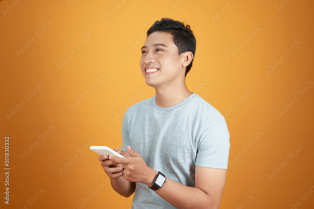 Portrait of a happy young asian man using mobile phone at studio on orange background. Portrait of a happy young asian man using mobile phone at studio on orange background.