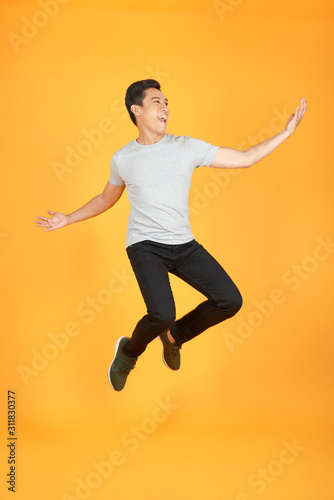 Energetic happy young Asian man in casual clothes jumping, studio shot isolated in orange background