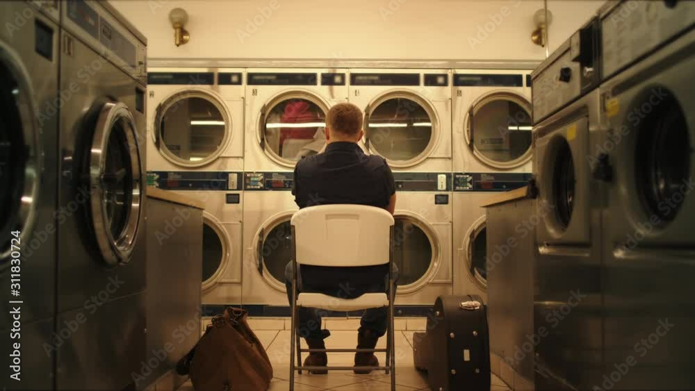 Man sits in laundry and waits clothes to wash, moment from everyday life, washing machines