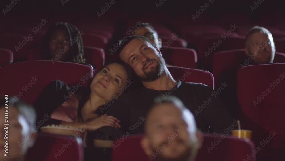 Tracking shot of affectionate woman and man sitting together in theater and watching movie Tracking shot of affectionate woman and man sitting together in theater and watching movie