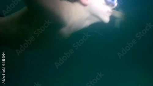 The guy in the bathing mask is swimming under water. The boy held his breath. Teen lifestyle rests or goes in for sports. Turbid water in the pool.