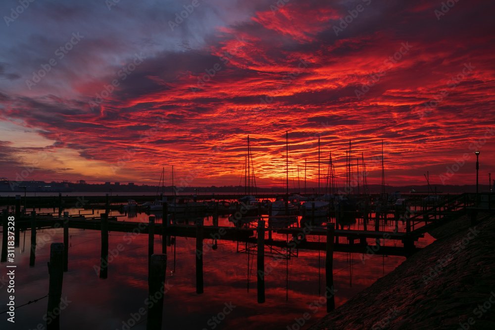 sail boats at the marina at dawn with dramatic fiery sky
