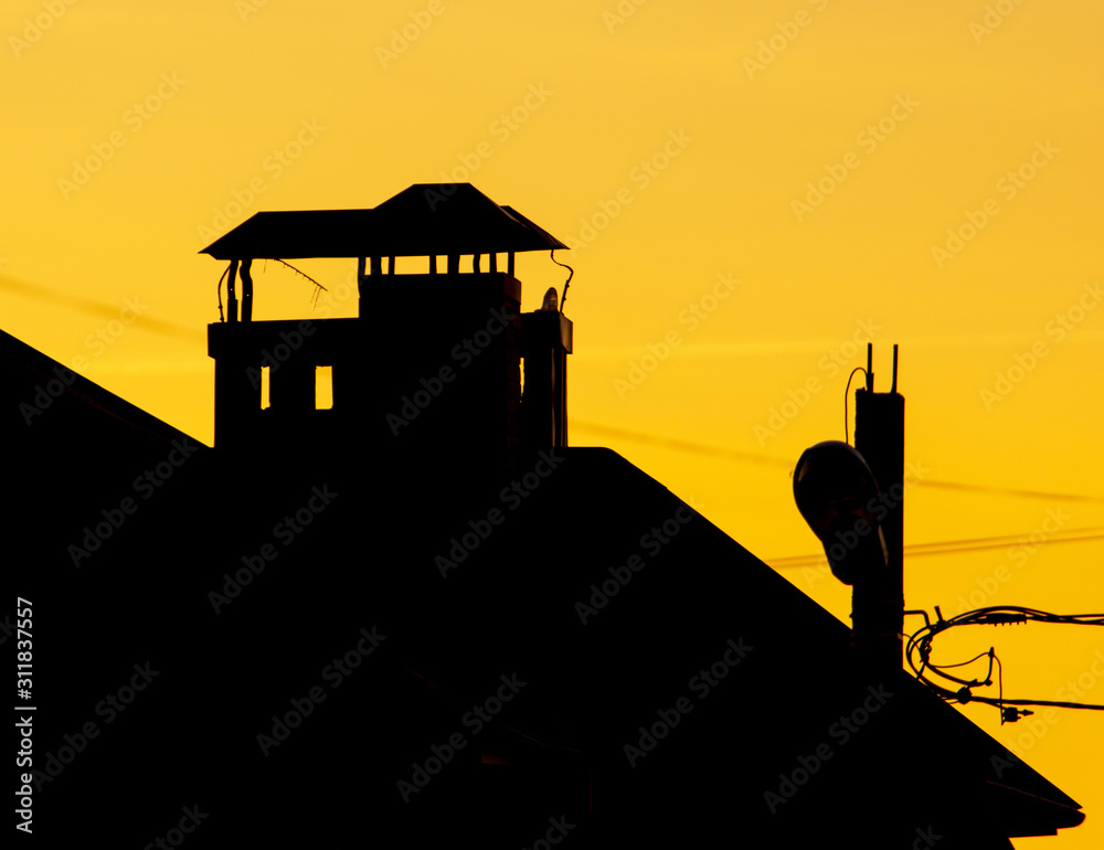 chimney on the roof of a house against the backdrop of a sunset