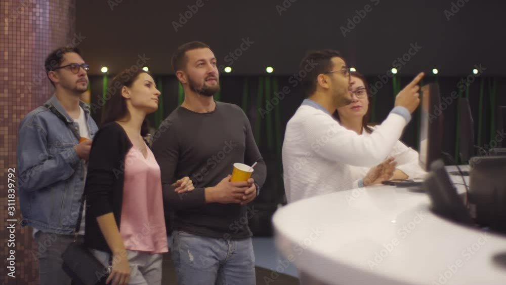 Tracking shot of people standing in line at cash register in cinema and buying movie tickets