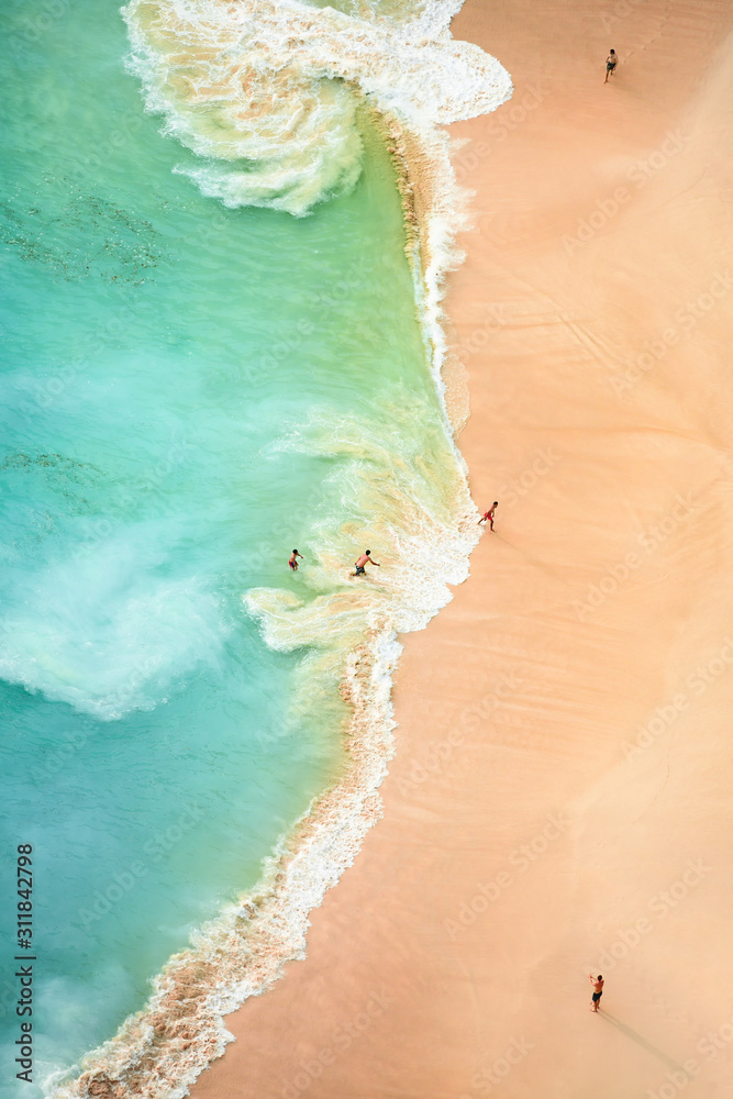 View from above, stunning aerial view of some tourists playing, sunbathing and swimming on a beautiful beach bathed by a turquoise sea during sunset. Kelingking beach, Nusa Penida, Indonesia.