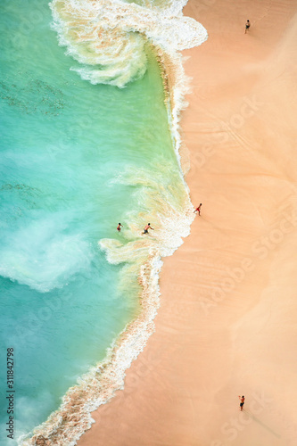 Obraz na płótnie View from above, stunning aerial view of some tourists playing, sunbathing and swimming on a beautiful beach bathed by a turquoise sea during sunset. Kelingking beach, Nusa Penida, Indonesia. w salonie