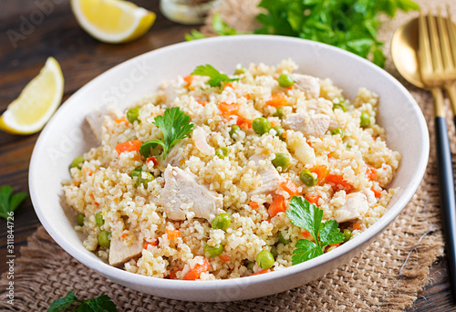 Bulgur with chicken, green peas and carrot on wooden background.