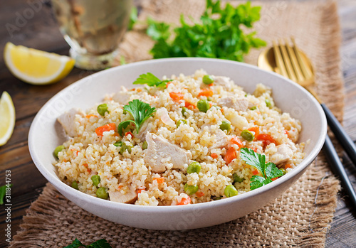 Bulgur with chicken, green peas and carrot on wooden background.