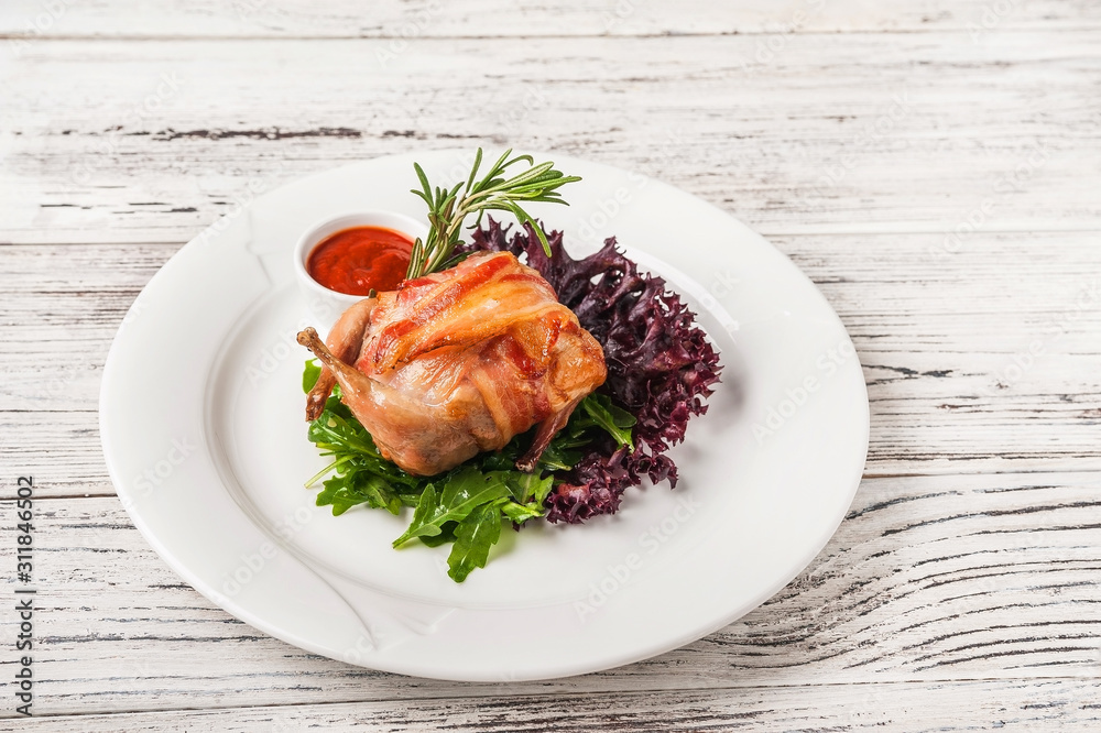 Quail stuffed in a restaurant close-up. Quail in bacon on a white plate and copy space. Quail stuffed in a restaurant close-up. Quail in bacon on a white plate and copy space.