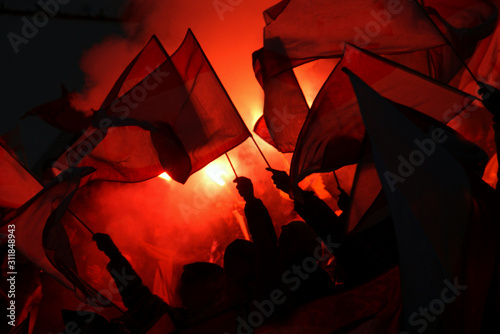 Silhouettes of sport fans holding flags with red pyrotechnical light in the background