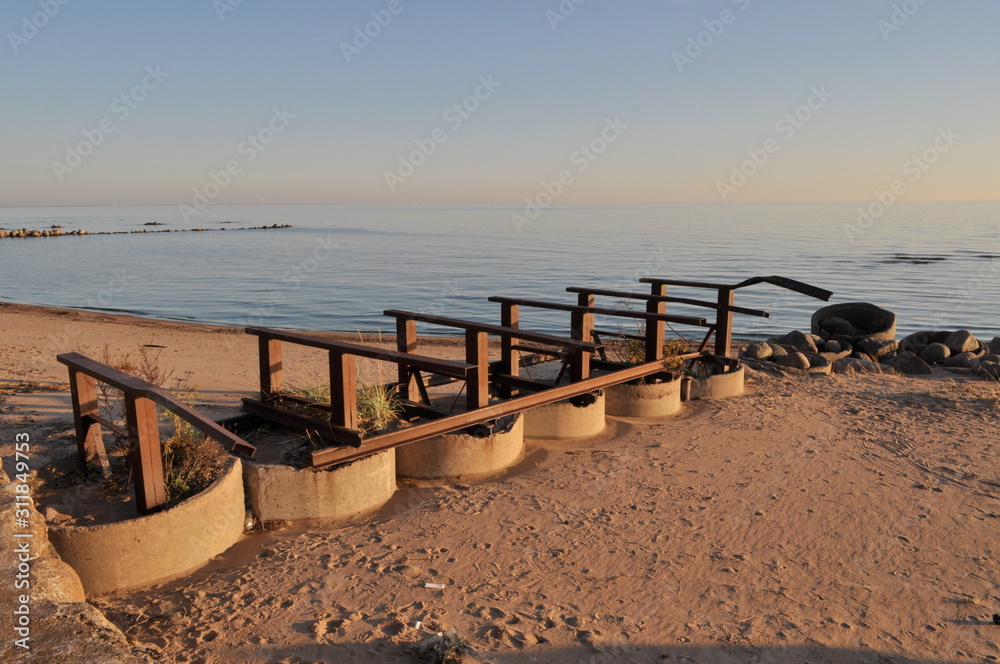 Photo of a beautiful landscape with soft sunset sunlight. Amazing blue sky, calm sea. In the foreground a fixture consisting of concrete rings and iron pillars