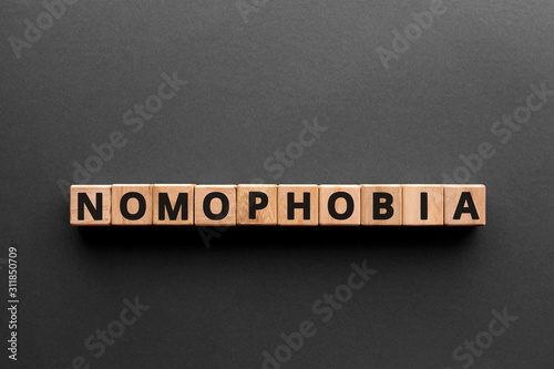 Nomophobia - word from wooden blocks with letters, phobia of being out of cellular phone contact nomophobia  concept, gray background