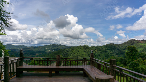 Scenery view from wooden terrace to white fluffy clouds on vivid blue sky above greenery mountain