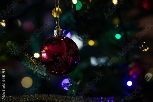 Red christmas ball hanging on a christmas tree with blurred lights on background